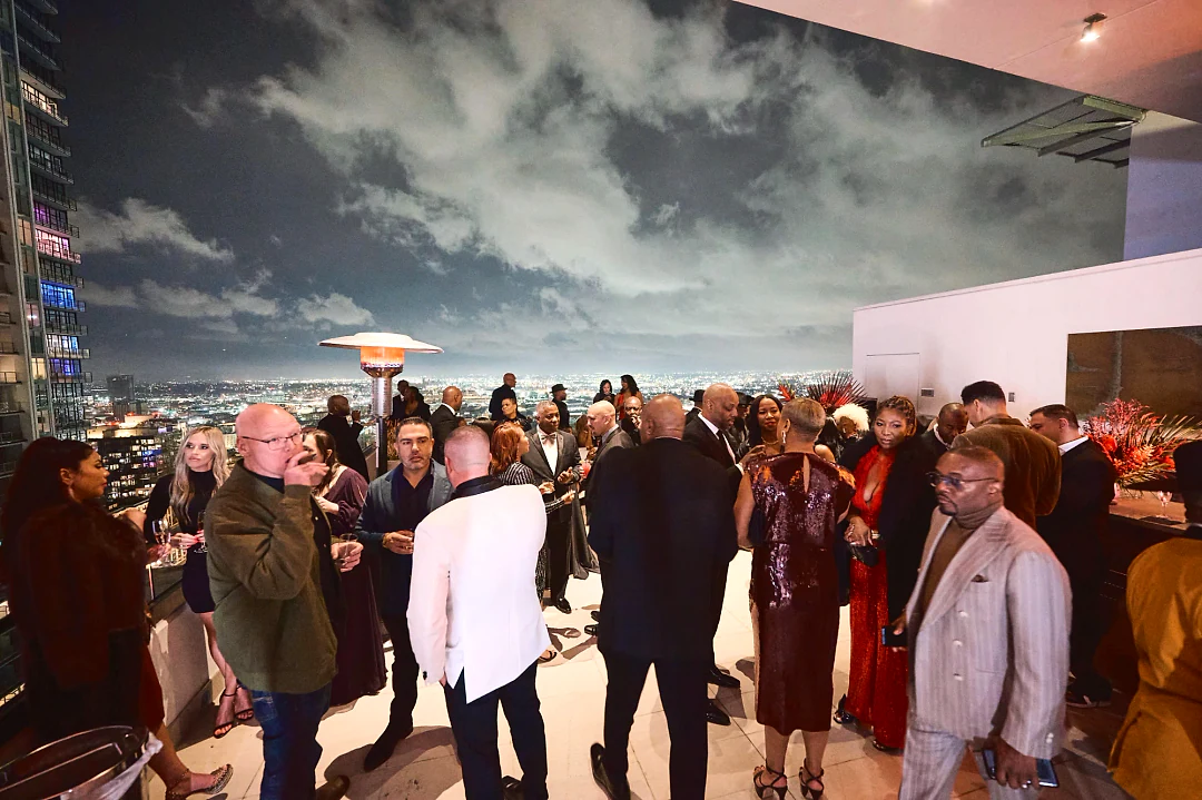 Guests gathered on a rooftop terrace at night above the city lights, one lighting a cigar