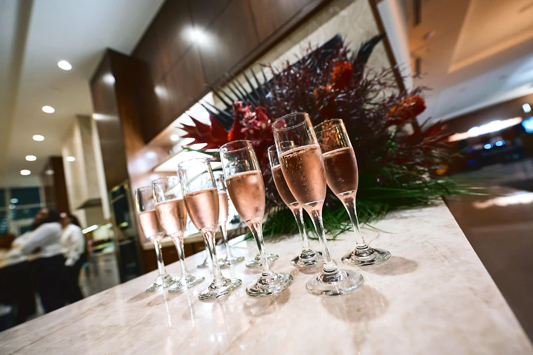 A row of rosé champagne flutes on a marble counter in front of red and orange flowers