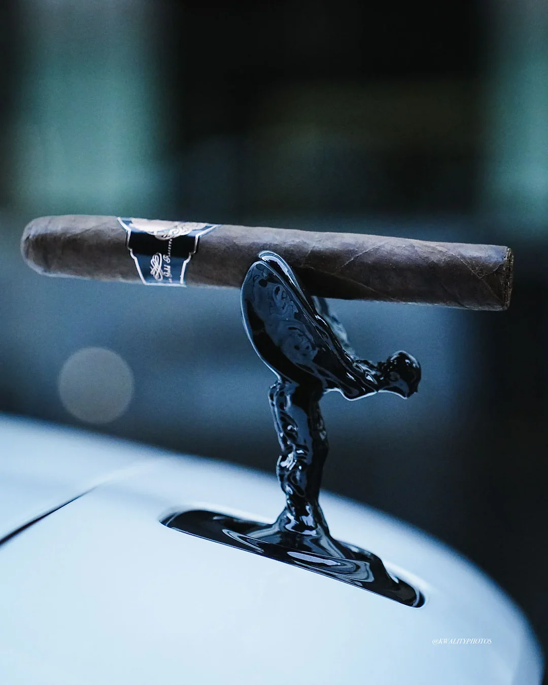 A Rose Gold Reserve cigar resting on a luxury car's hood ornament